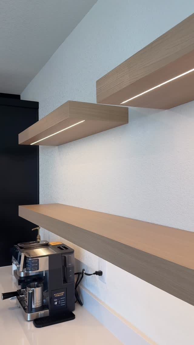 Modern coffee station with light wood floating shelves and integrated under-shelf lighting.