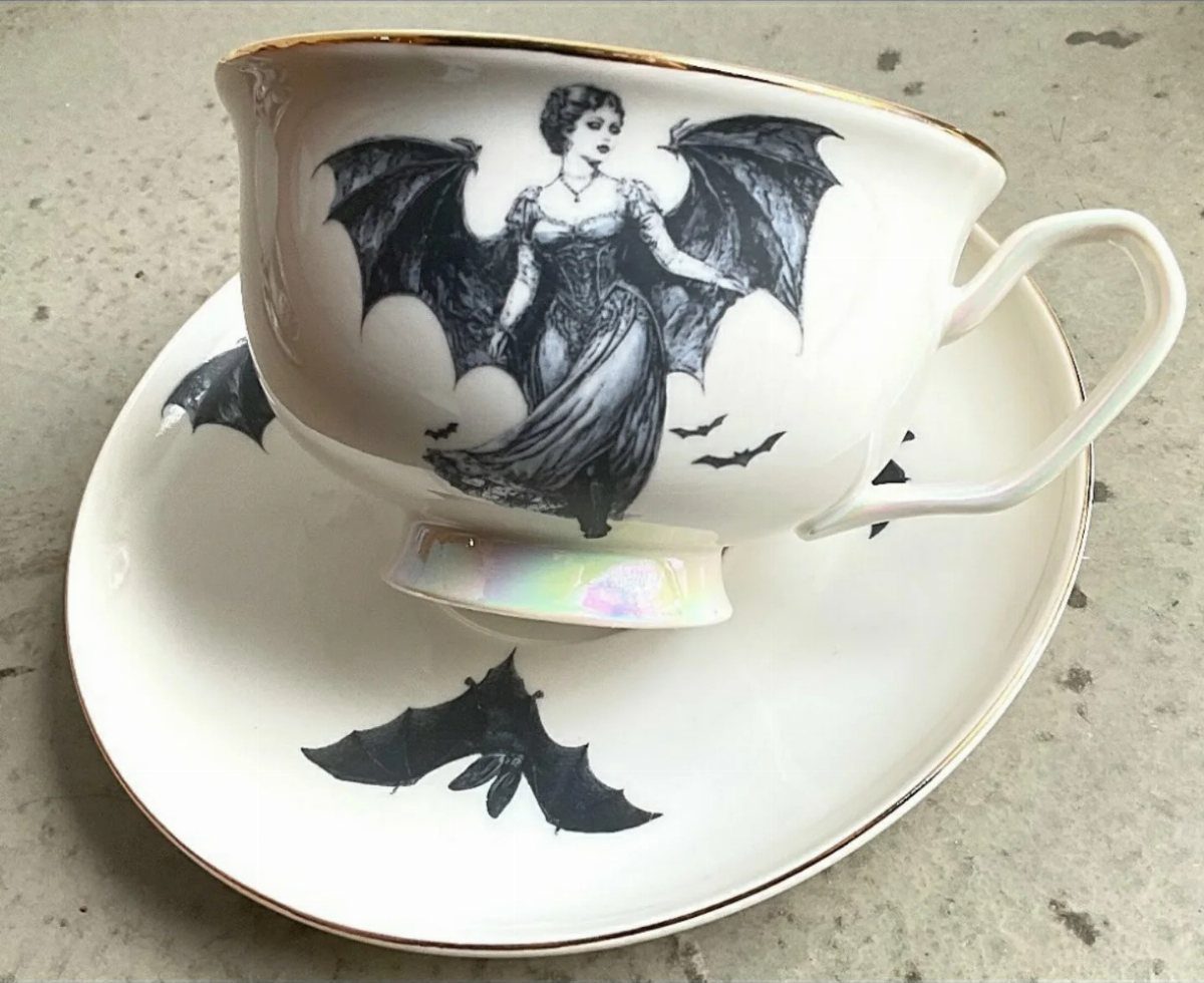 Gothic Tea Set: 24 Dark & Elegant Serving Ideas 21 White teacup and saucer featuring black illustrations of a bat-winged woman and bats.