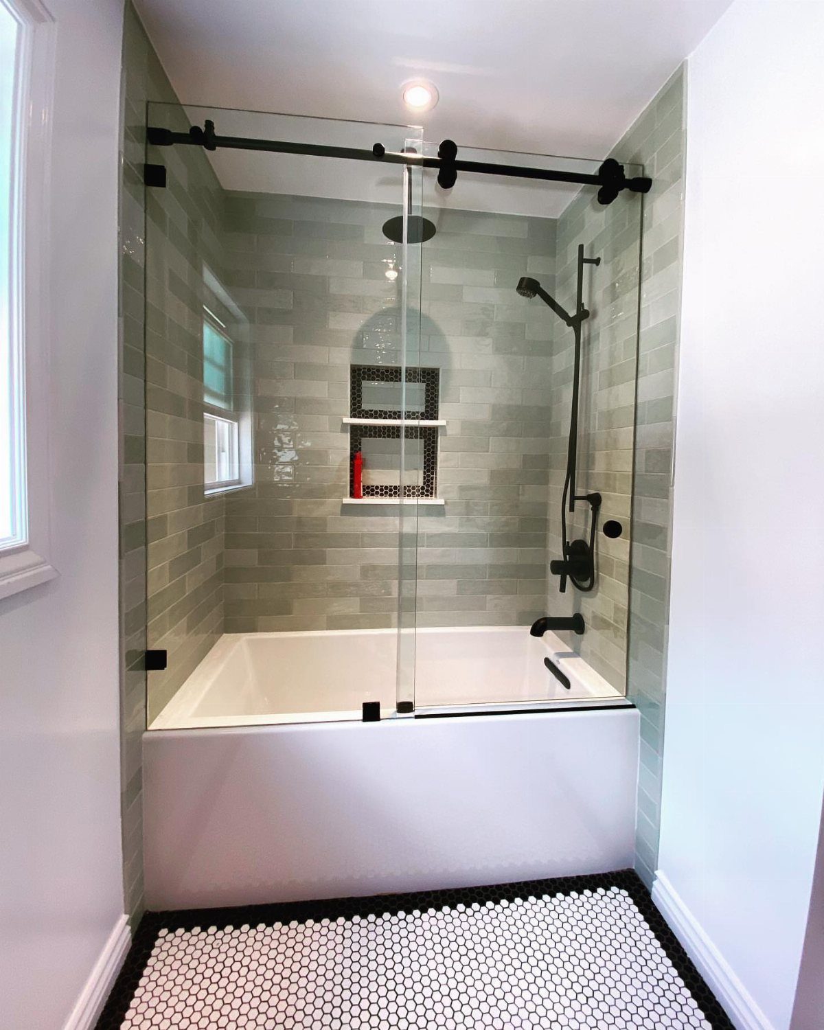 White bathtub with glass sliding doors and grey tile walls in a bathroom.