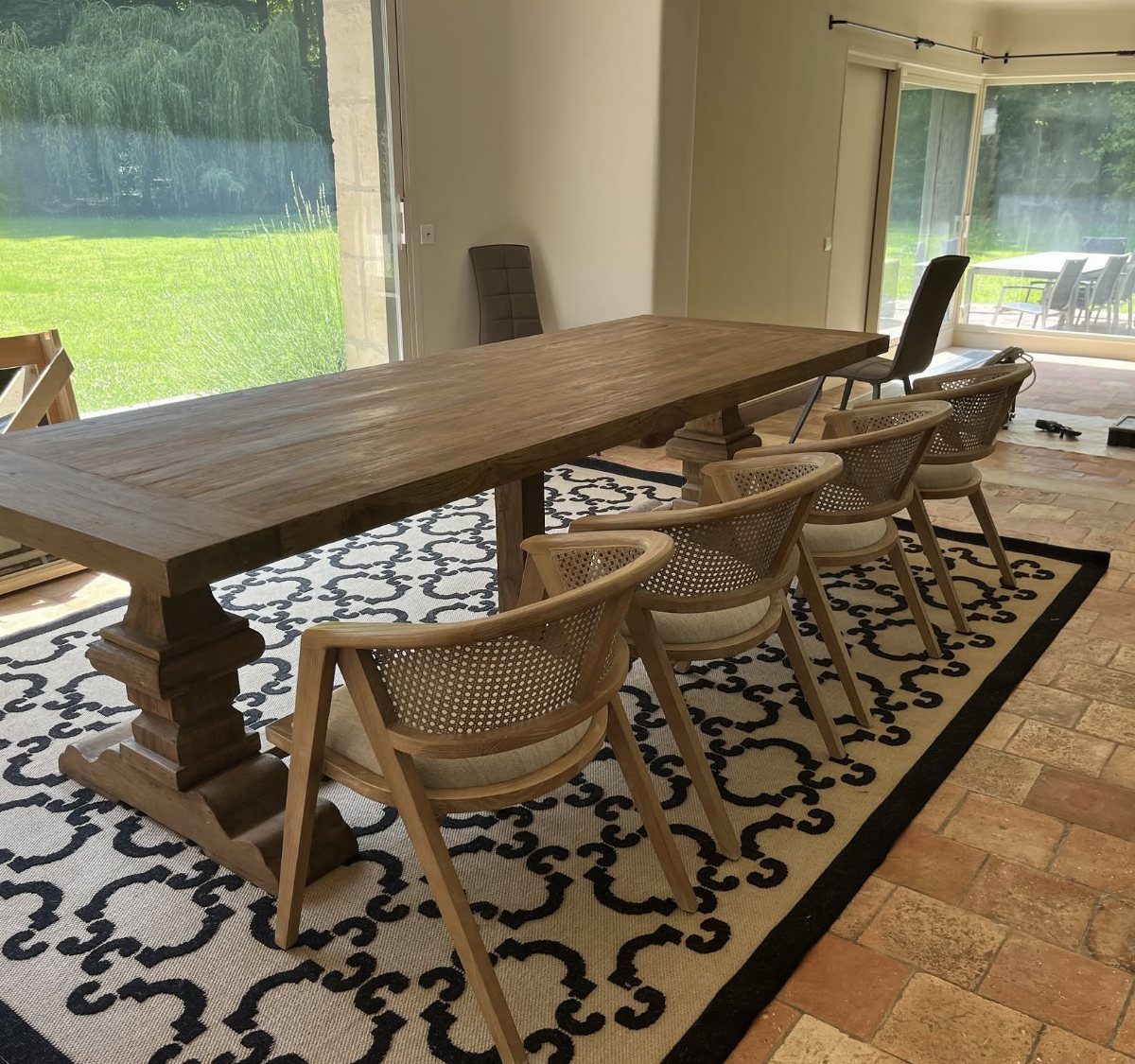 20 French Farmhouse Dining Table Ideas for Every Style 6 Light brown wooden monastery table with cane-back chairs on a patterned rug.