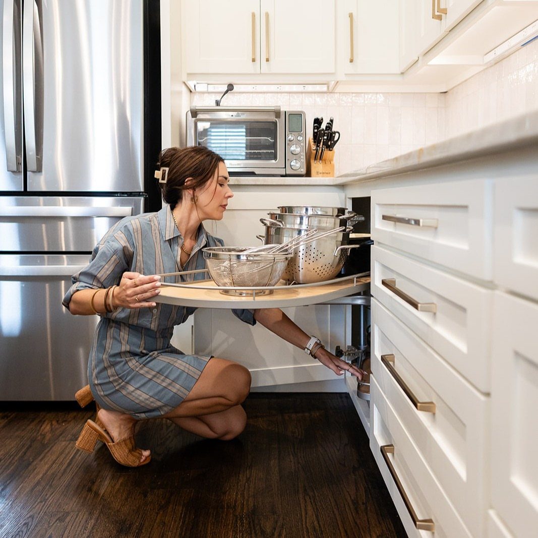 Woman pulling out a curved blind-corner pullout shelf filled with metal pots.