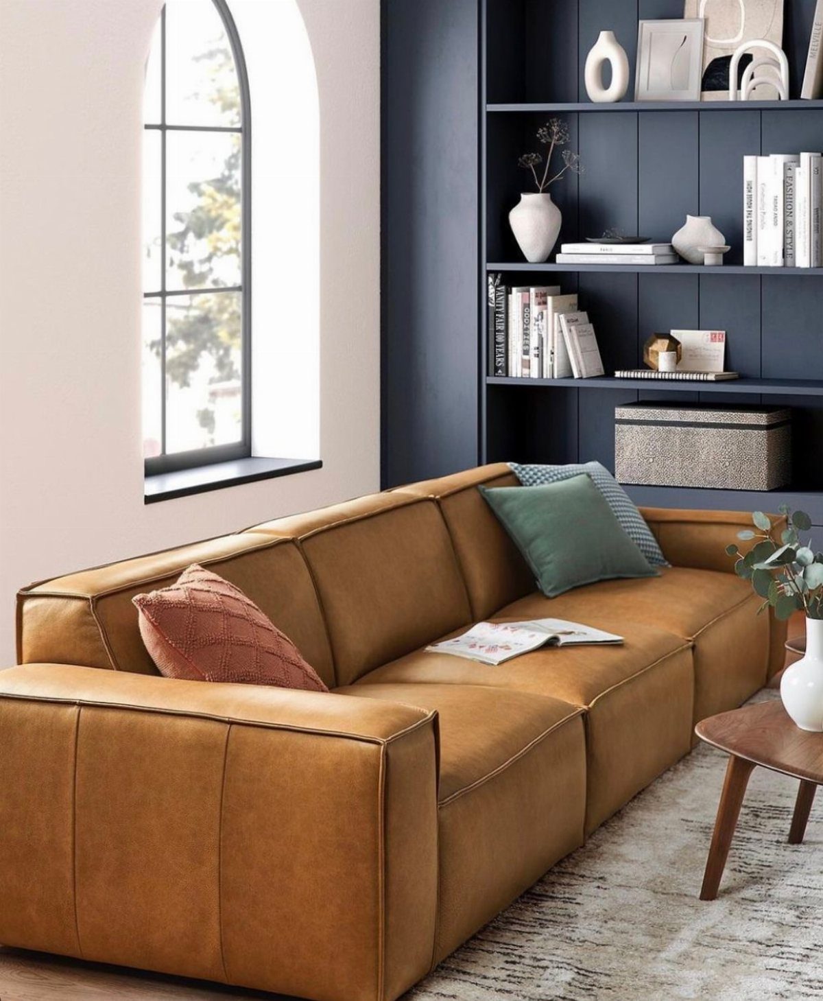 Brown leather sofa in a living room with dark blue shelving and arched window