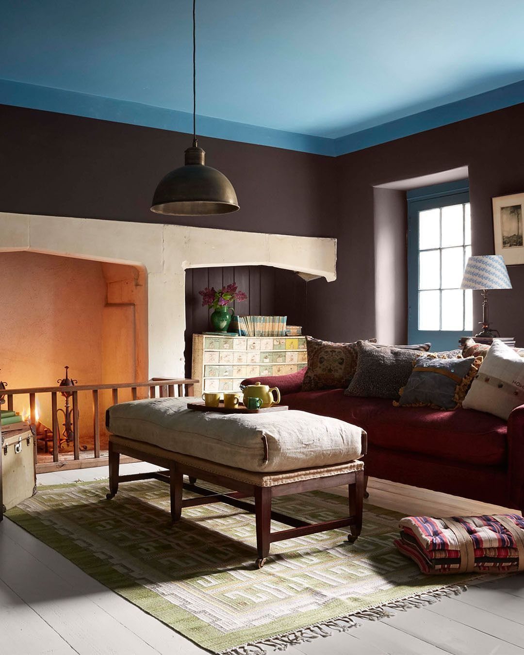 Living room with dark brown walls, blue ceiling, red sofa, and stone fireplace.