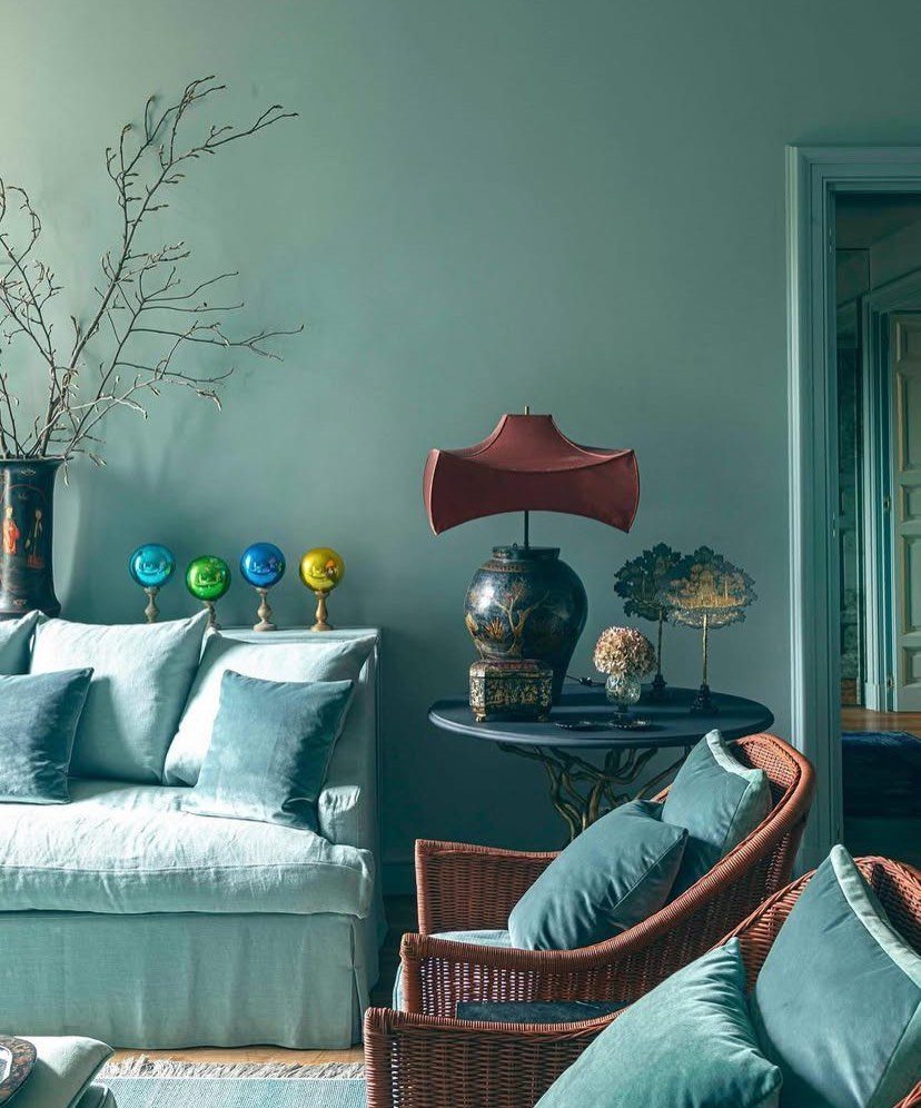 Blue sofa and brown wicker chairs in a room with blue-green walls.