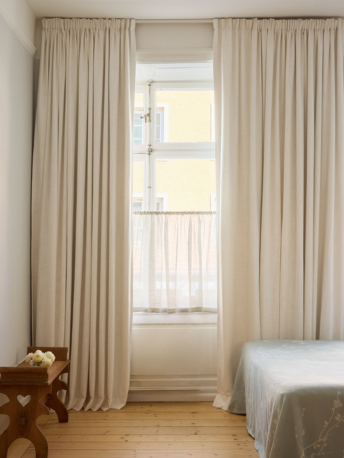 Cream curtains and a sheer cafe curtain on a bedroom window.