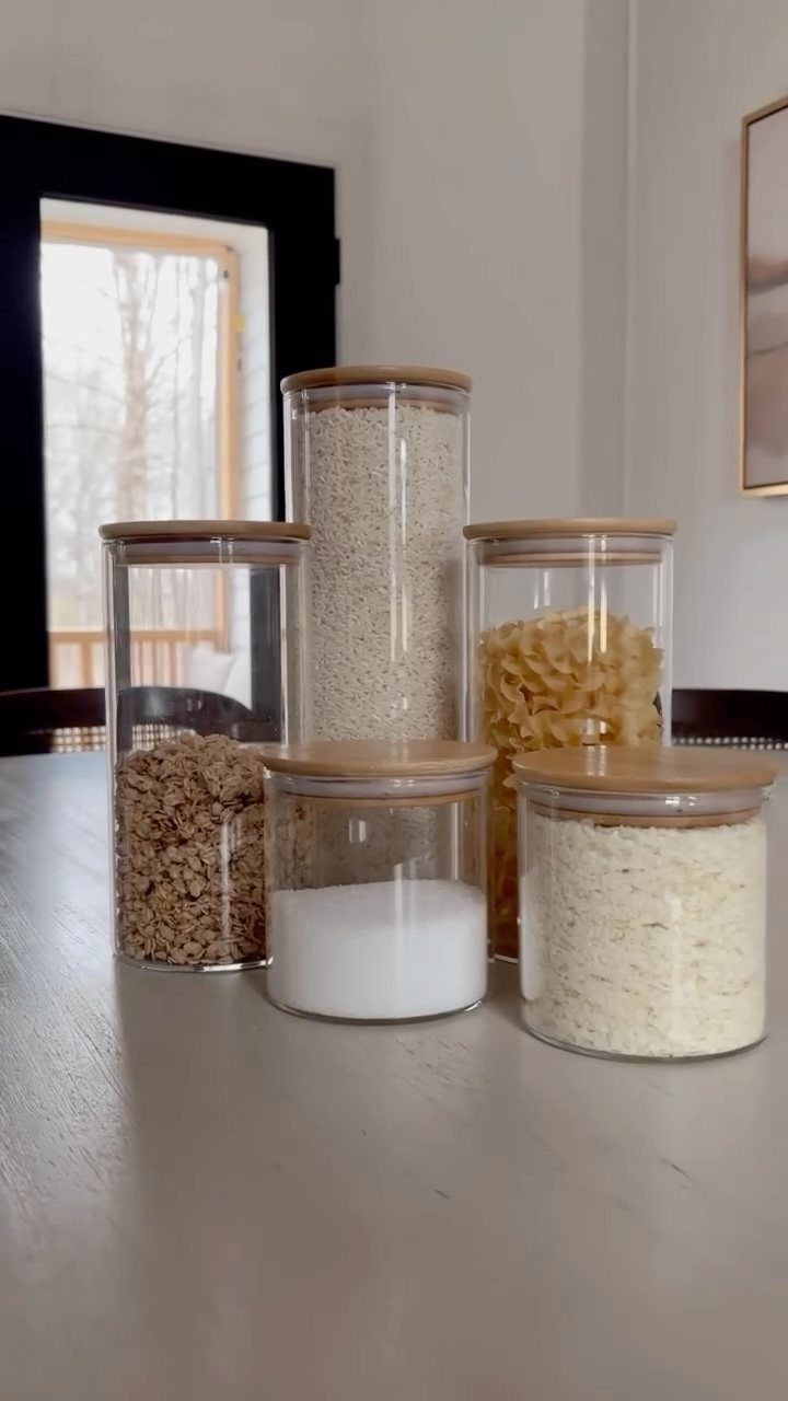 Clear glass jars with bamboo lids filled with various dry pantry staples.