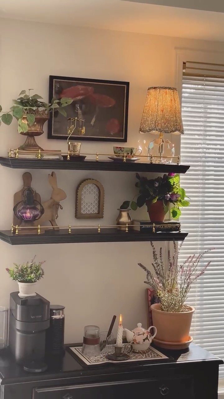Coffee station with a black sideboard and floating shelves decorated with various potted plants.