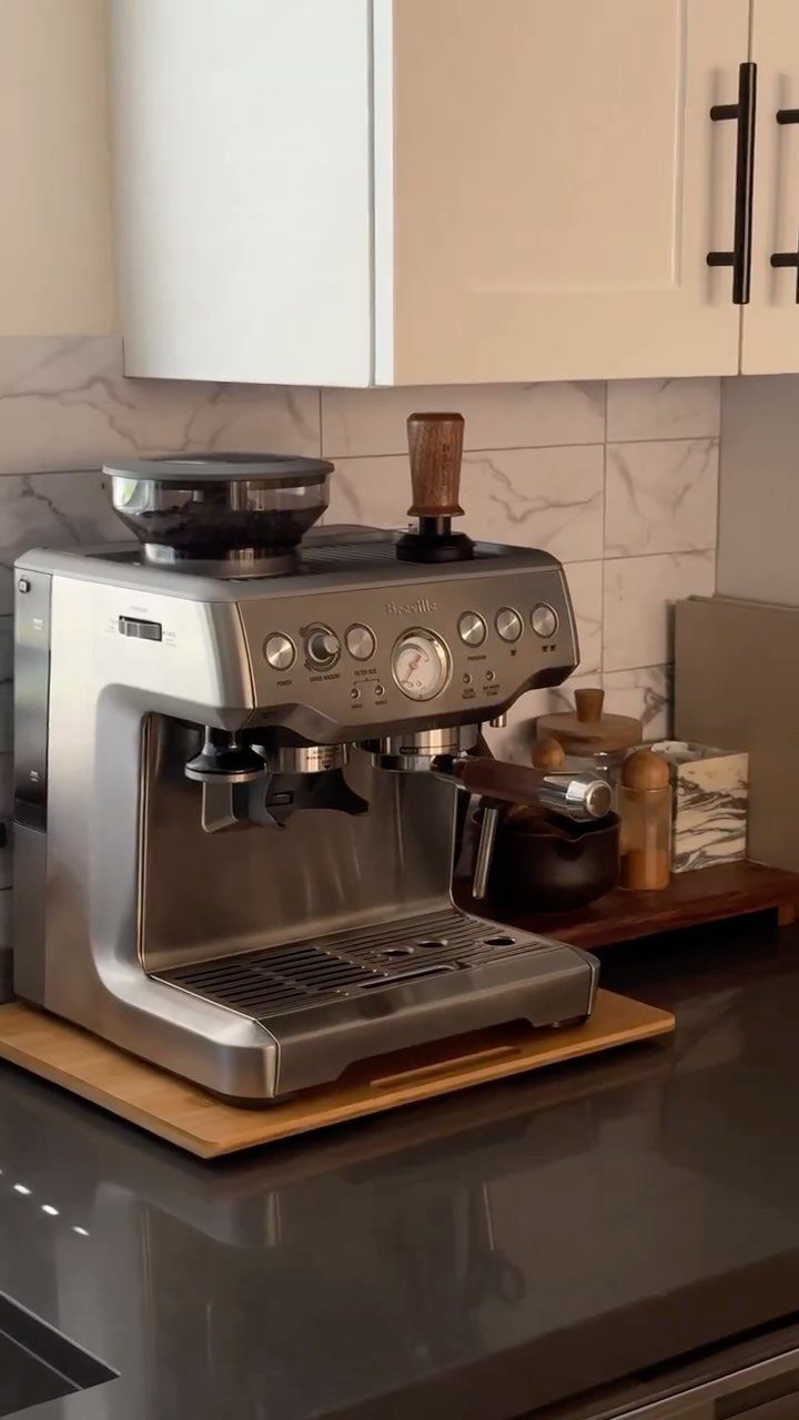 Silver espresso machine on a light wood tray atop a grey kitchen countertop.