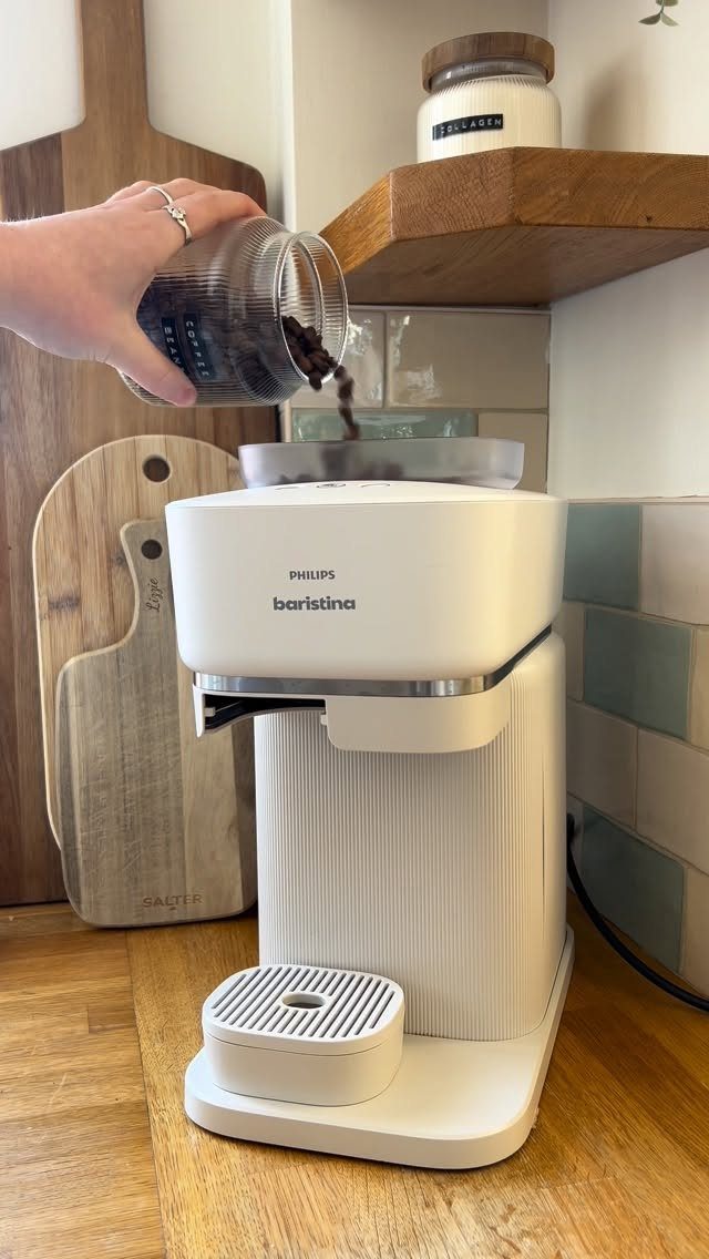 White Philips Baristina coffee machine being filled with coffee beans from a glass jar.