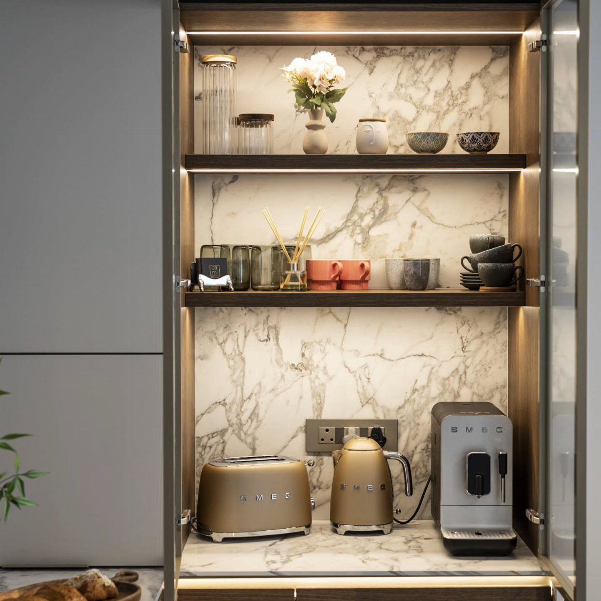 Coffee and tea bar with gold appliances and marble backsplash inside a cabinet.