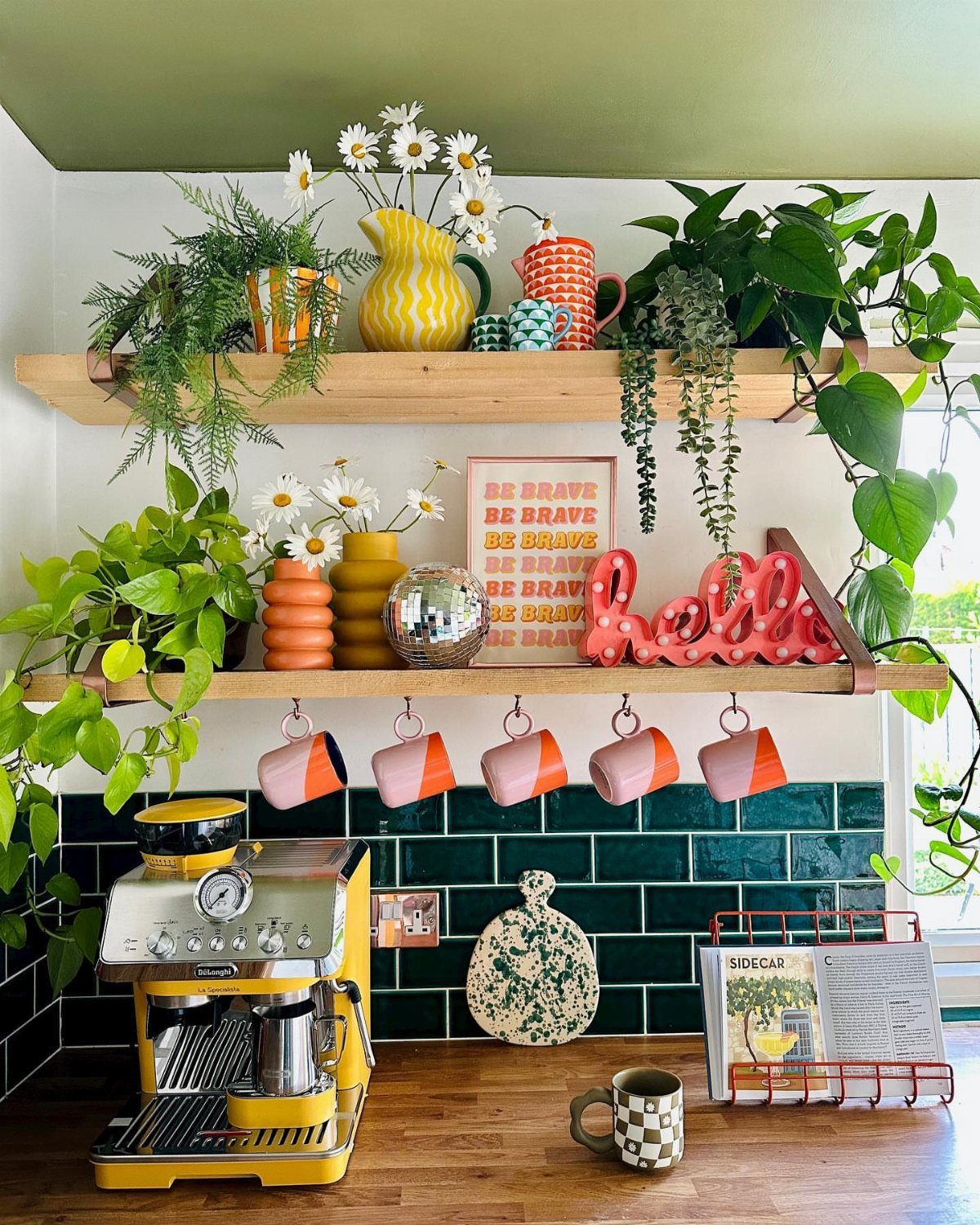 Colorful coffee bar with yellow espresso machine, green tiles, and bright decorative mugs.