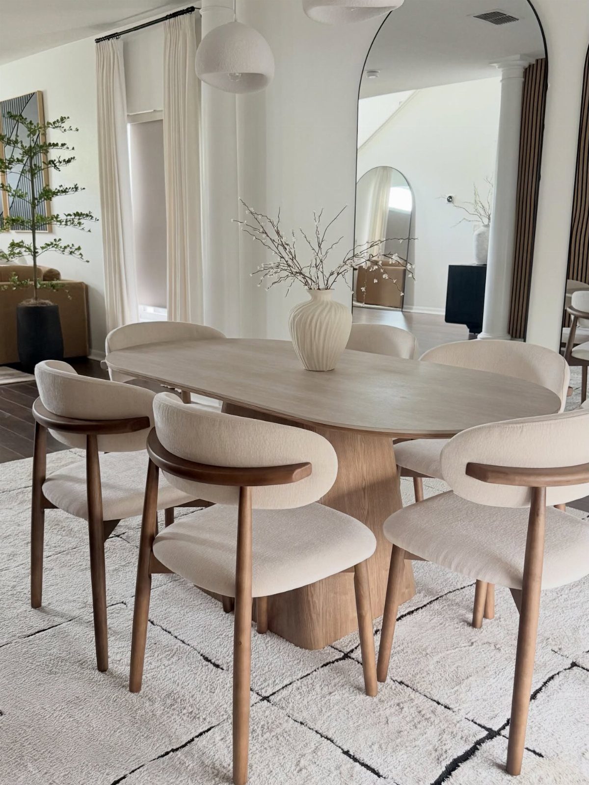 Oval light-wood dining table with cream upholstered chairs in a bright modern room