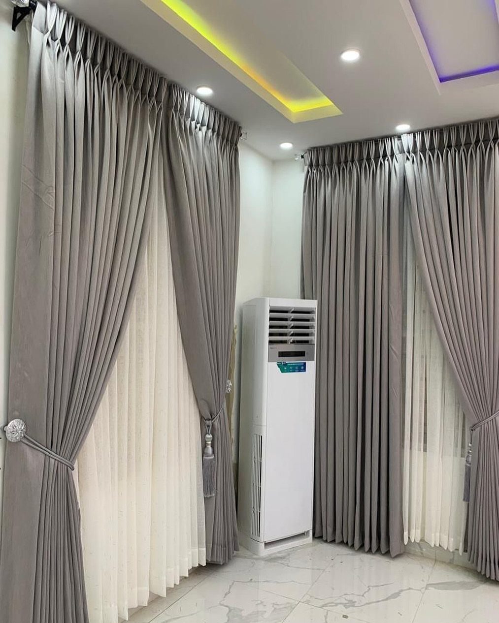 Grey and white double-layered curtains extending beyond the window frames in a white room.