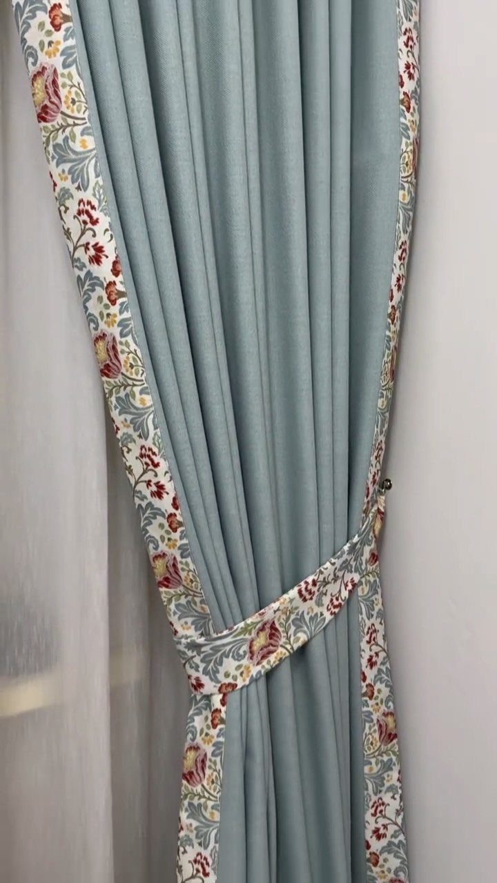 Light blue curtains with floral borders held back by a matching fabric tieback.