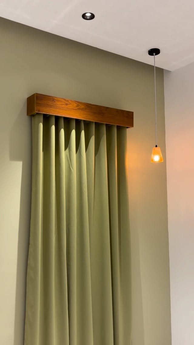 Olive green curtains with a wooden valance hanging against a neutral wall.