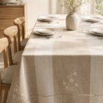Beige striped linen tablecloth with floral embroidery on a set dining table.