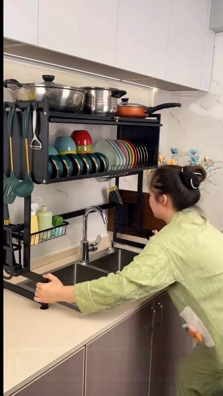Black metal over-the-sink dish rack holding plates and pots in a modern kitchen.