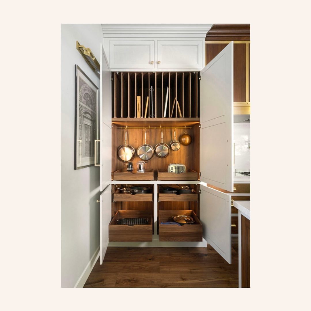 White pantry cabinet with vertical wooden dividers for baking sheets and copper pots.