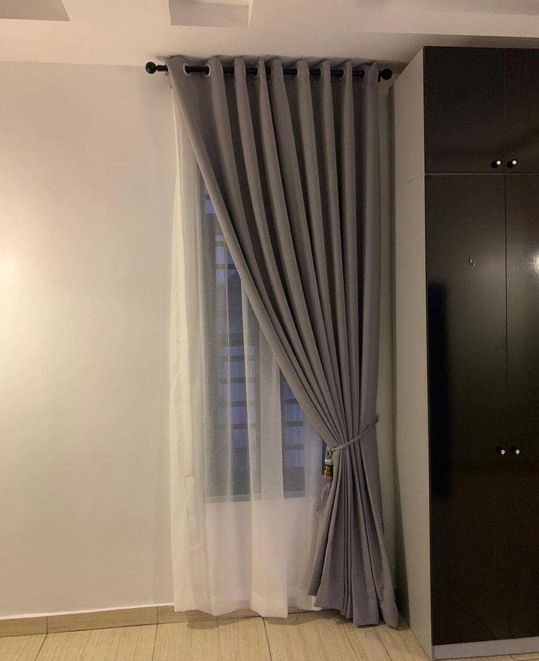 Grey and white curtains hanging over a short window in a bedroom
