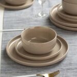 Beige porcelain bowl and plates stacked on a grey textured tablecloth with gold cutlery.