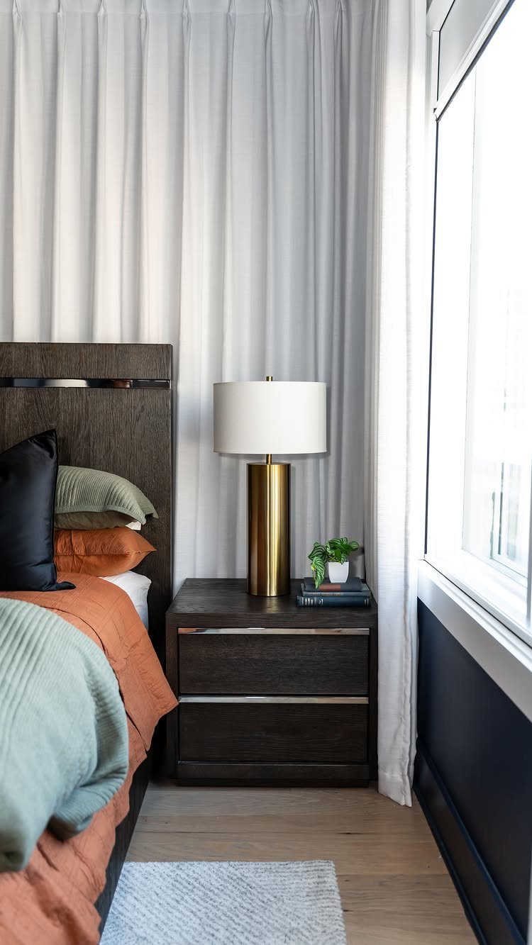 White curtains hanging in a bedroom next to a dark wood nightstand and bed.