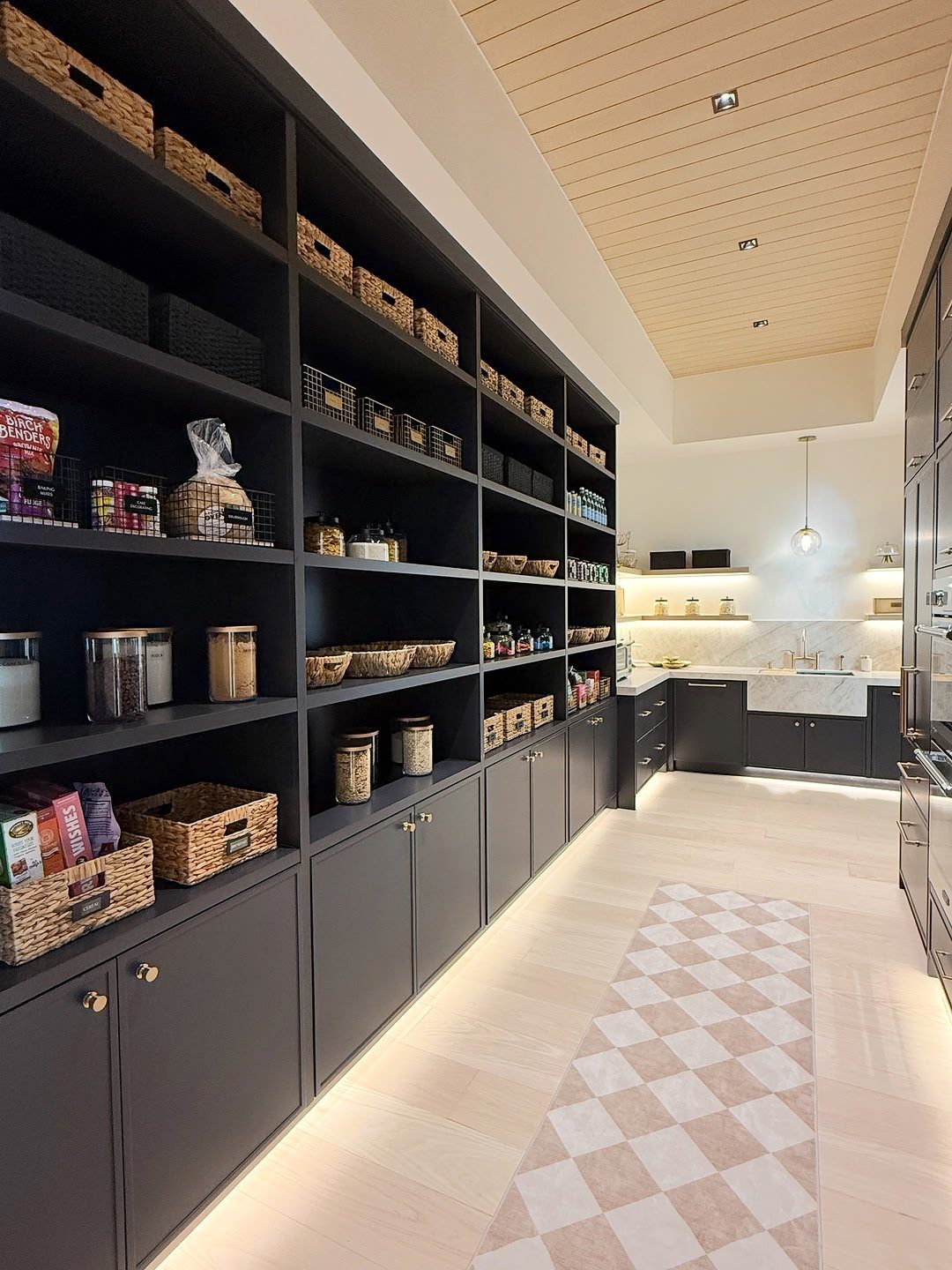 Dark grey built-in pantry shelves with organized baskets and containers in a bright kitchen.