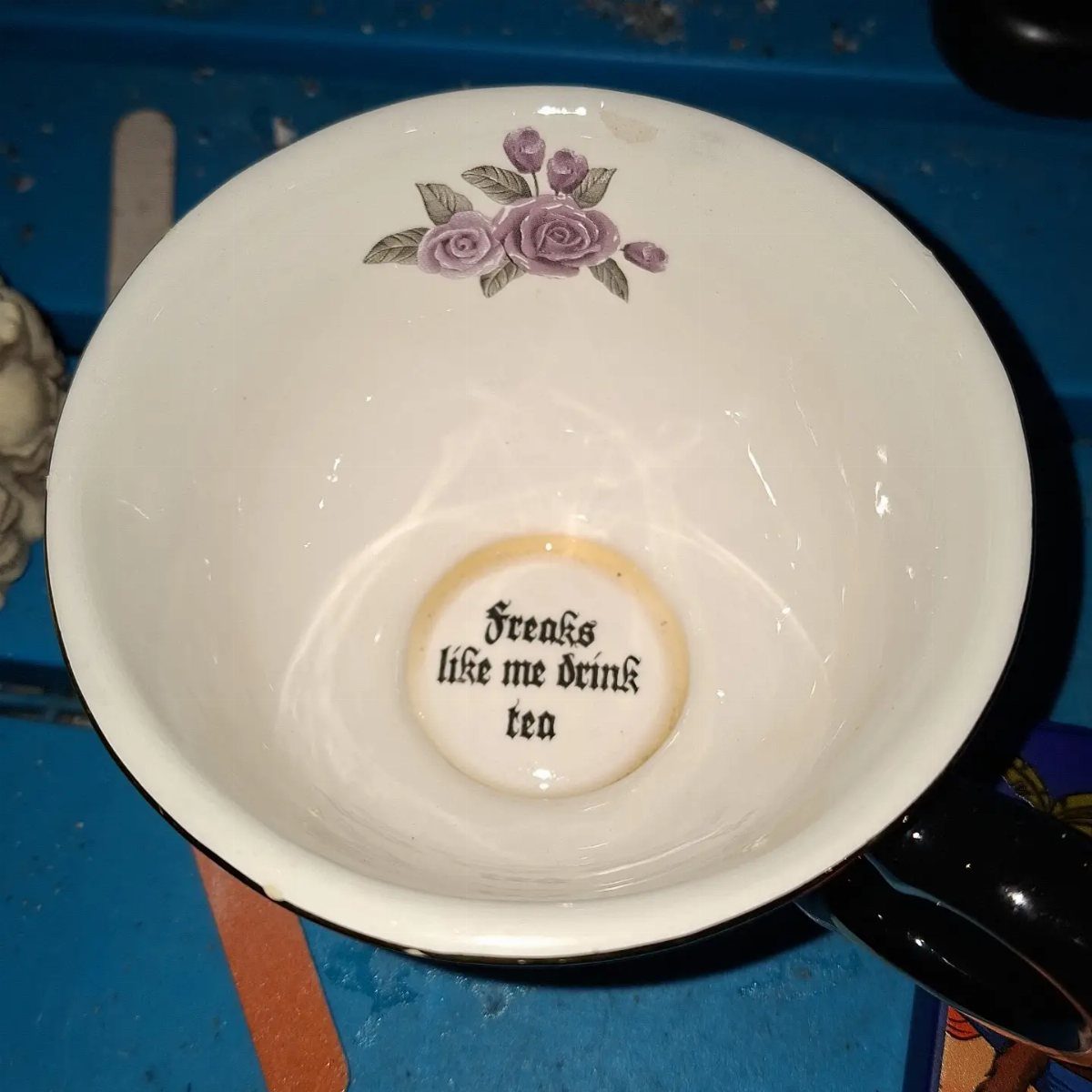 Gothic Tea Set: 24 Dark & Elegant Serving Ideas 22 White teacup interior with purple roses and gothic text on the bottom.
