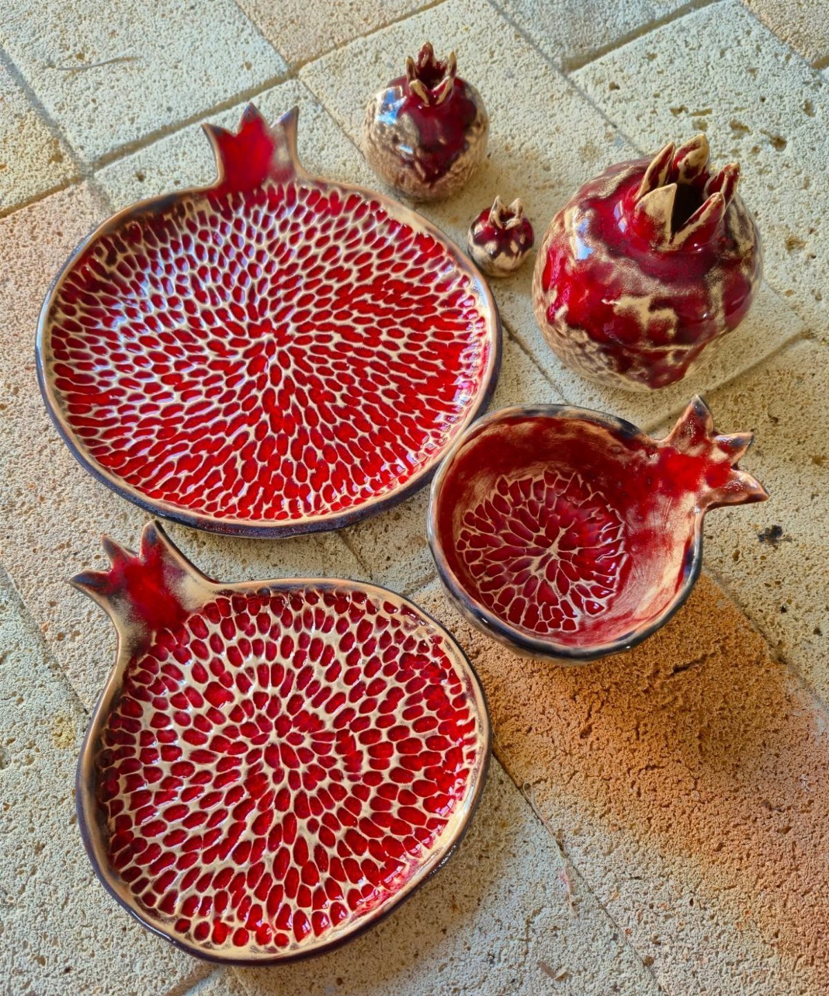 Fruit Shaped Plates in 12 Styles 5 Pomegranate shaped ceramic plates and figurines with red textured interiors on stone tiles.