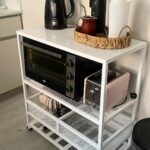 White rolling kitchen cart holding a toaster oven, pink toaster, and electric kettle.