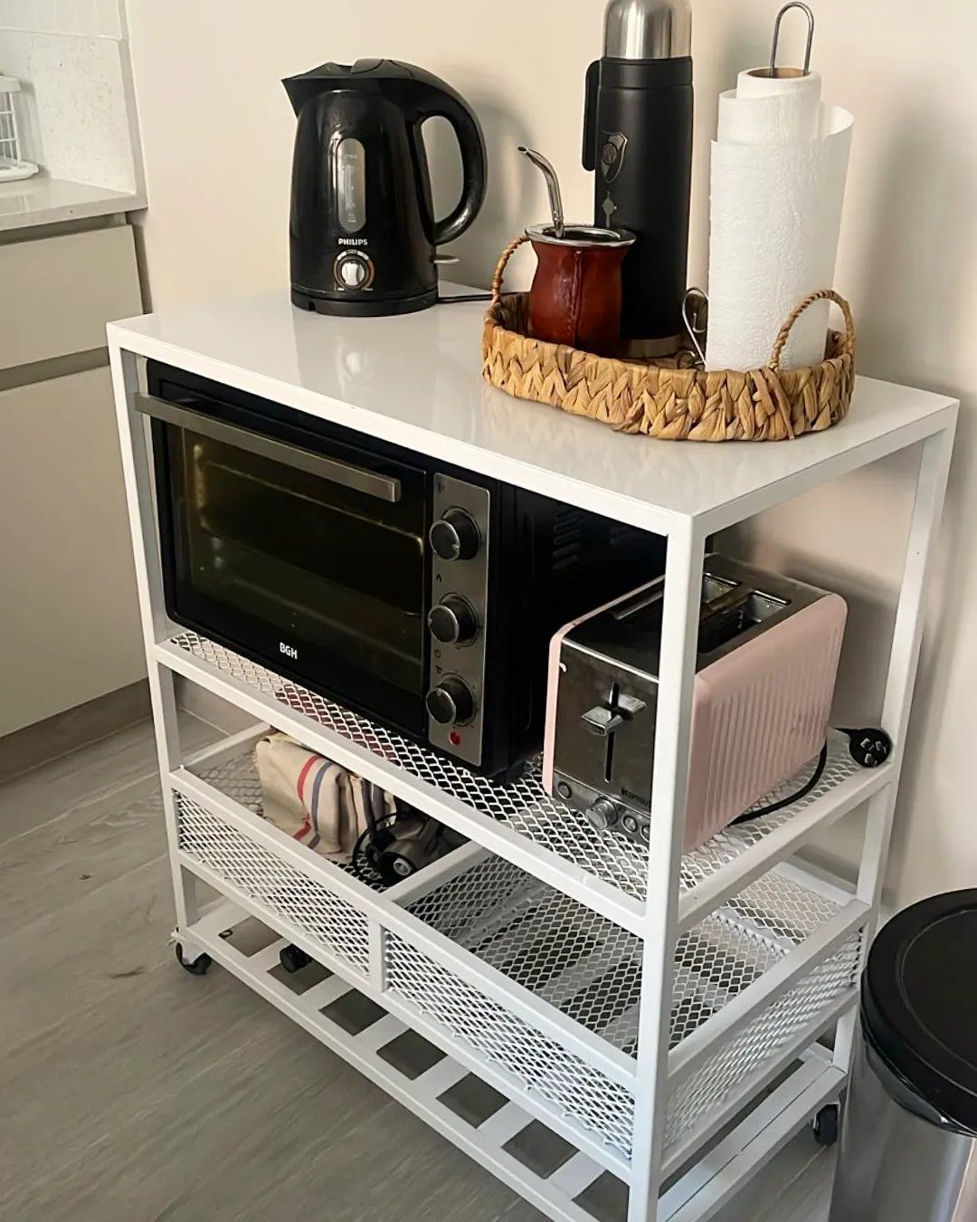 White rolling kitchen cart holding a toaster oven, pink toaster, and electric kettle.