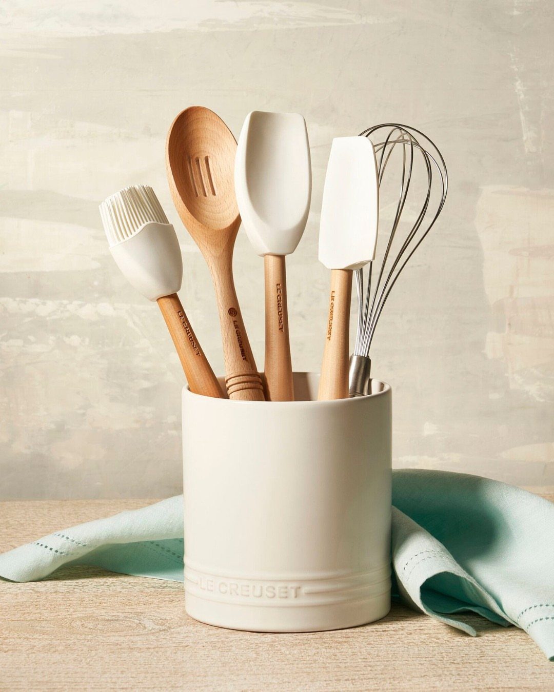 White ceramic utensil crock holding various kitchen tools on a light wooden countertop.