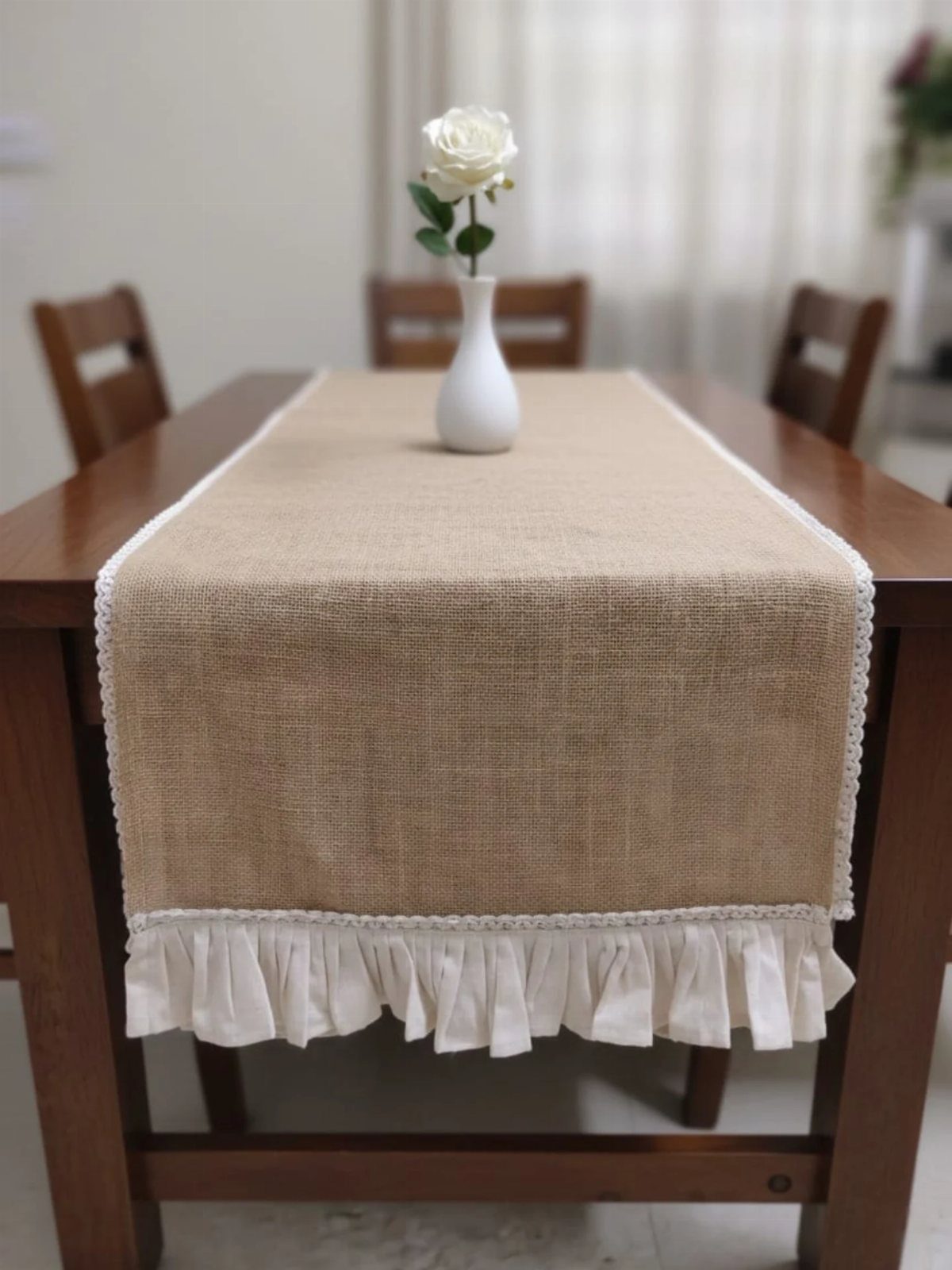 Jute table runner with white lace and ruffles on a wooden dining table.