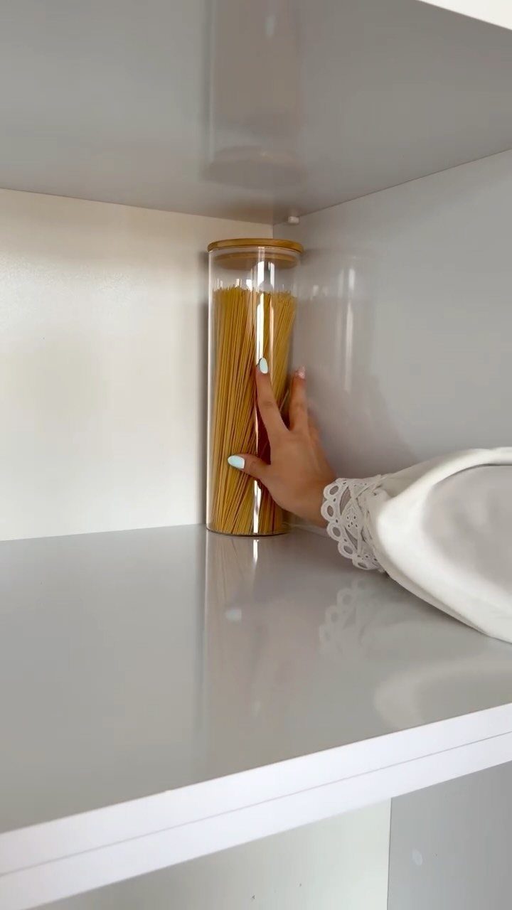 Clear glass canister filled with spaghetti pasta on a white kitchen shelf.