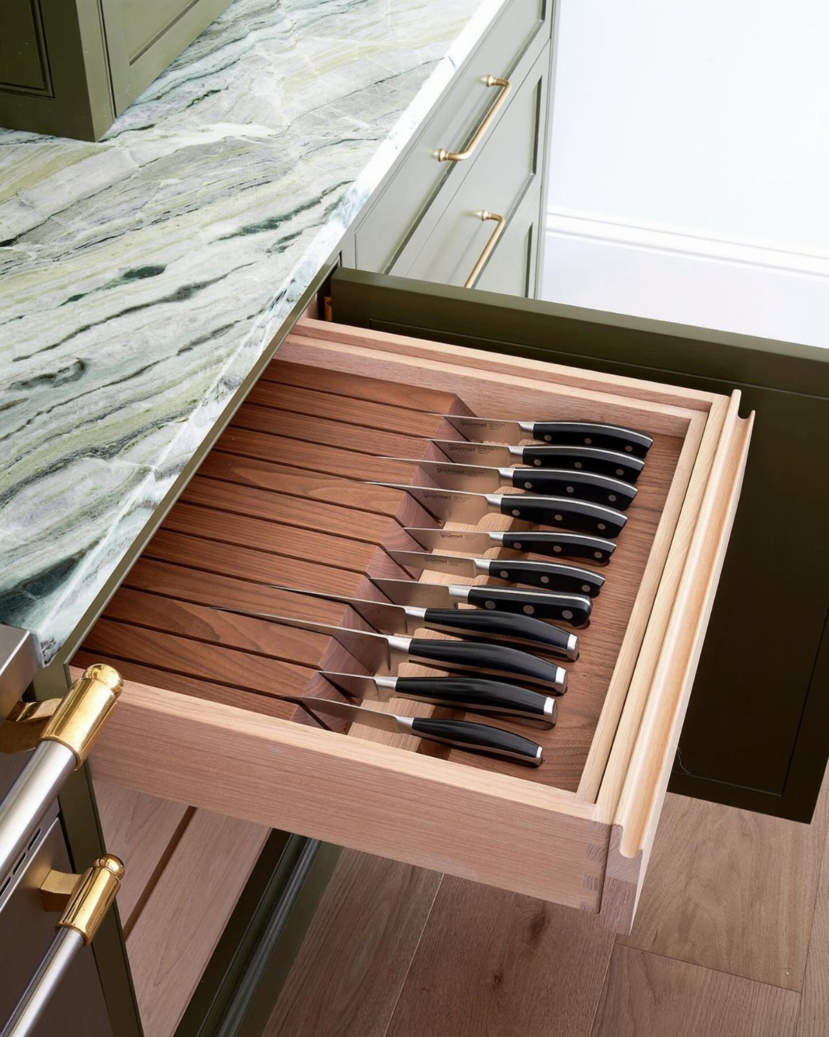 Wooden kitchen drawer with a built-in organizer holding several black-handled knives.