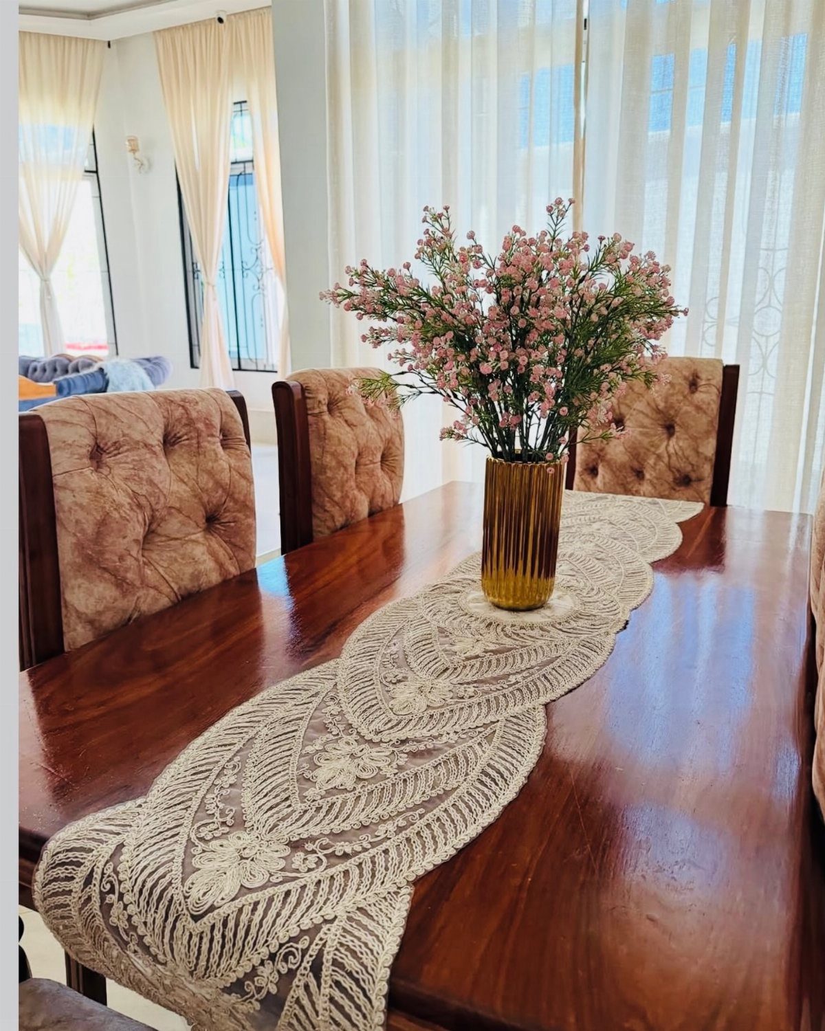 White lace table runner on a dark wood dining table with pink flowers.