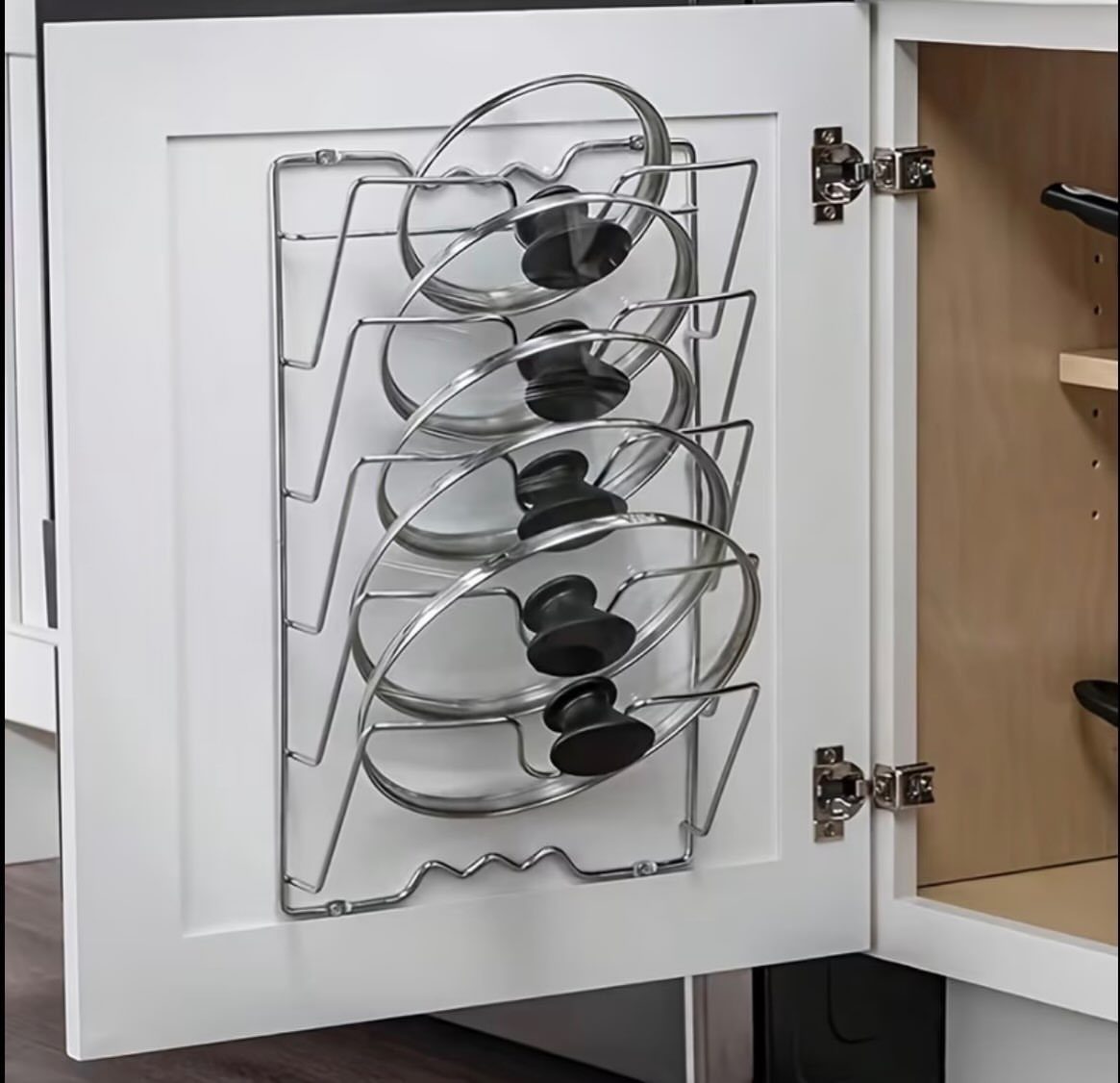 Metal wire rack mounted on a white cabinet door holding glass pot lids.
