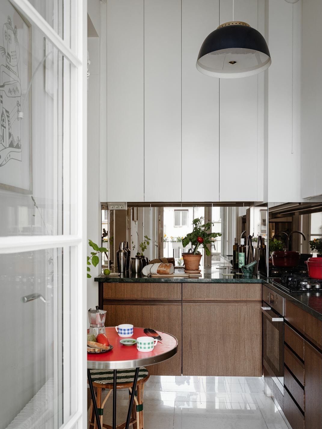 Small kitchen with white cabinets and a mirrored backsplash reflecting the room.