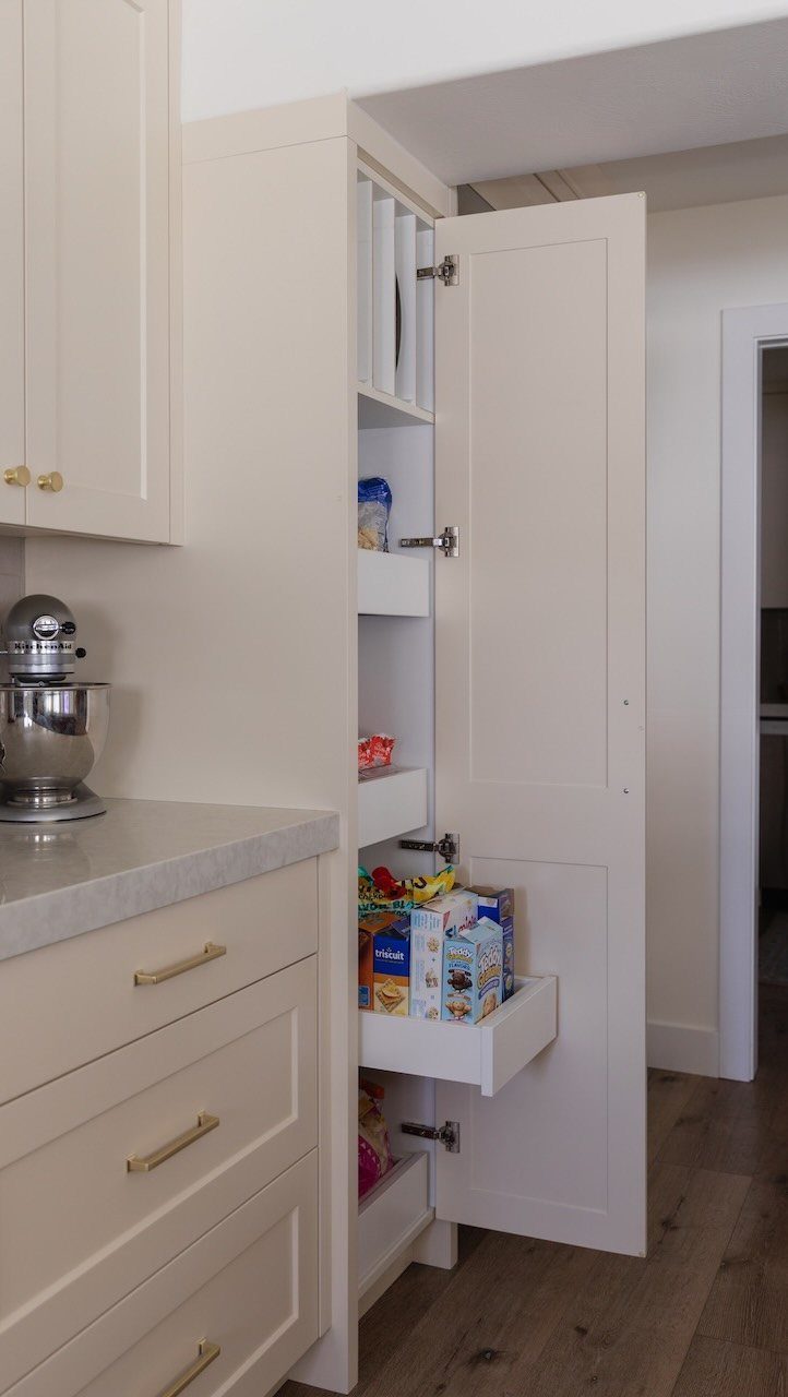 White narrow pantry cabinet with open door and pull-out drawer holding cereal boxes.