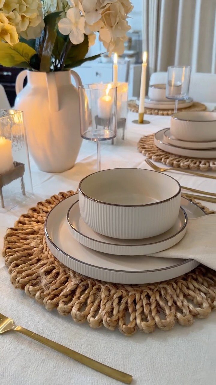 White tablecloth with woven jute placemats, white dinnerware, and cream flowers in vase.
