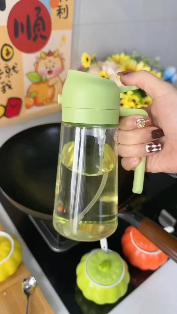 Glass oil dispenser with light green lid held over a black frying pan.