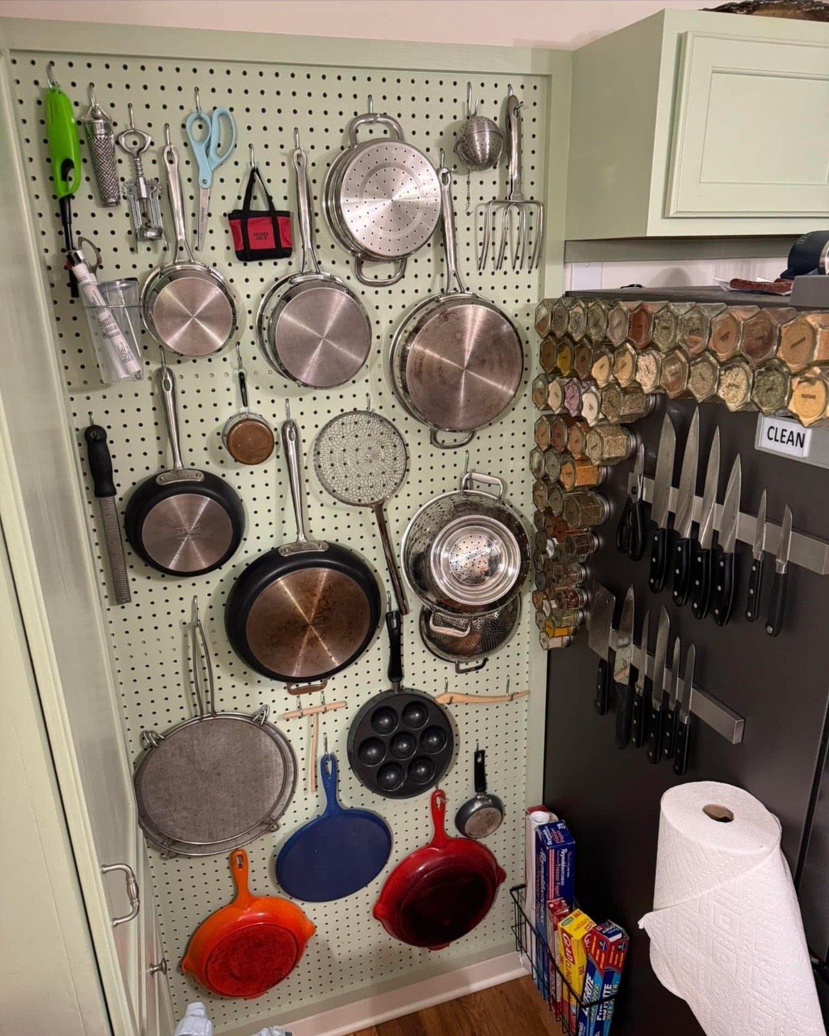 White pegboard holding various pots, pans, and kitchen utensils on a kitchen wall.