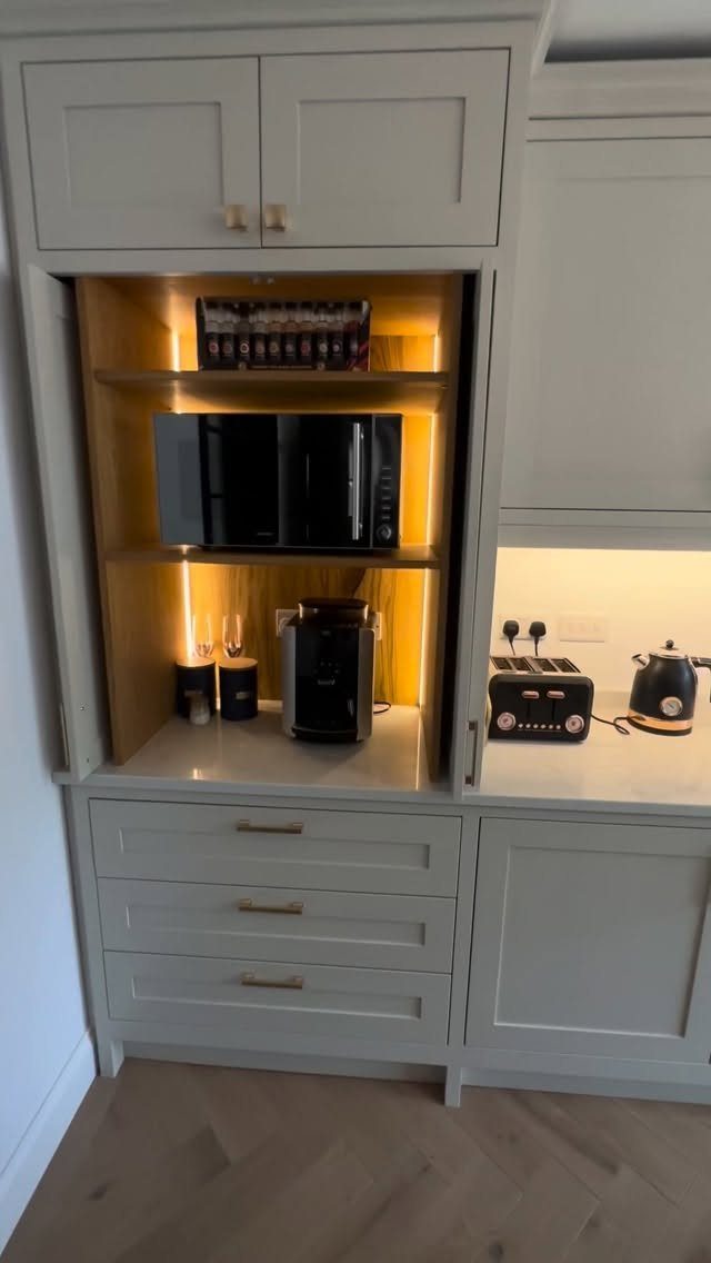 Grey kitchen cabinet with pocket doors open to reveal a coffee station and microwave.