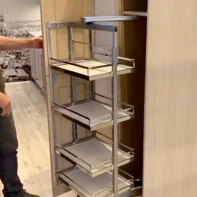 Pull-out metal shelving unit inside a light wood kitchen cabinet for pantry organization.