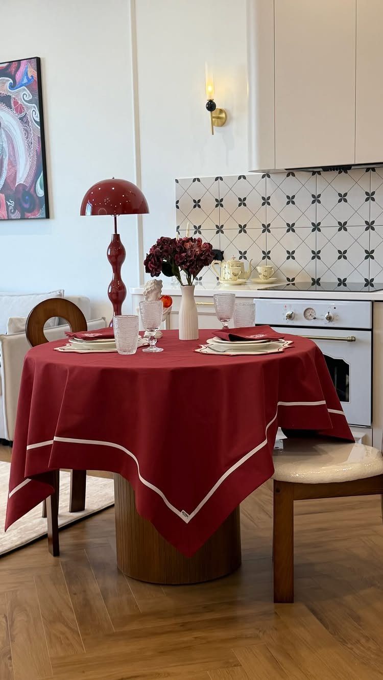 Red tablecloth with white trim on a round dining table with white plates.