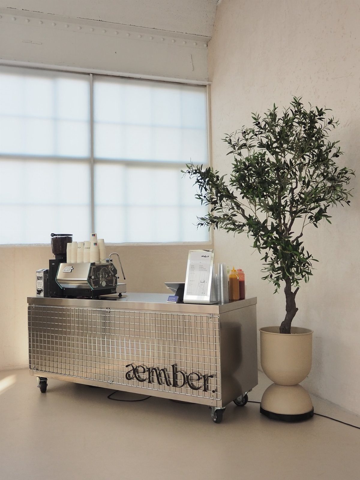 Metallic rolling coffee cart with an espresso machine next to a potted plant.