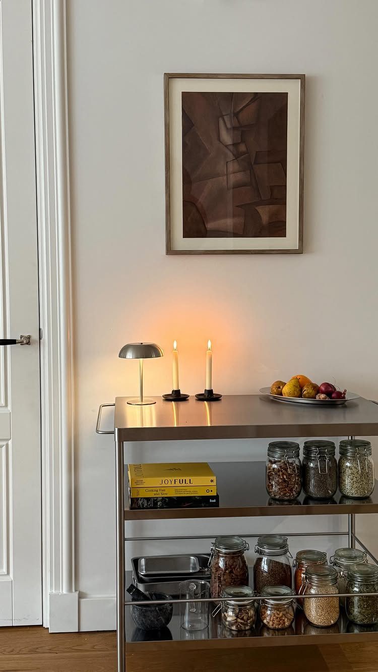 Silver metal cart with glass jars of grains and seeds against a white wall.