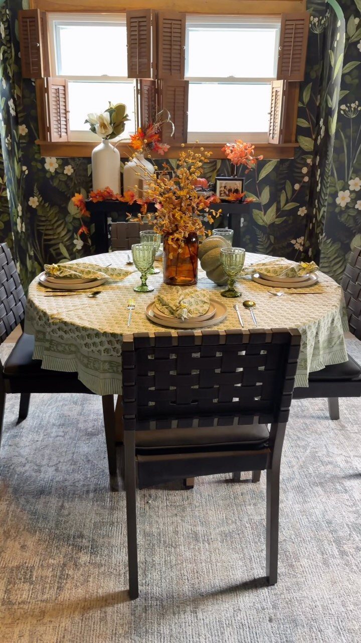 Round dining table with light green patterned tablecloth, glassware, and floral centerpiece.