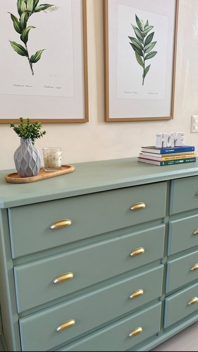 Sage green painted dresser with gold handles and botanical art on the wall