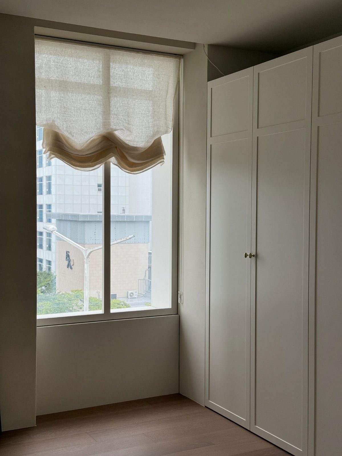 White semi-transparent curtains on a short window next to a white wardrobe.