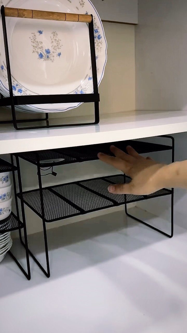Black metal wire shelf riser holding white floral plates on a white kitchen shelf.